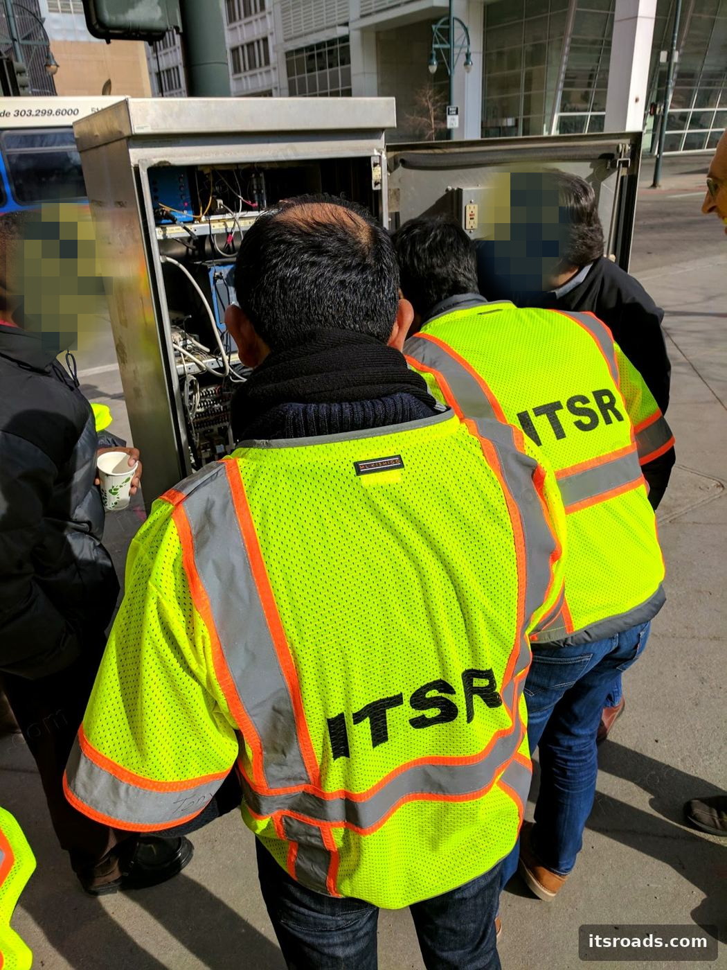 ITS Roads crew in safety vests reviewing an open roadside cabinet