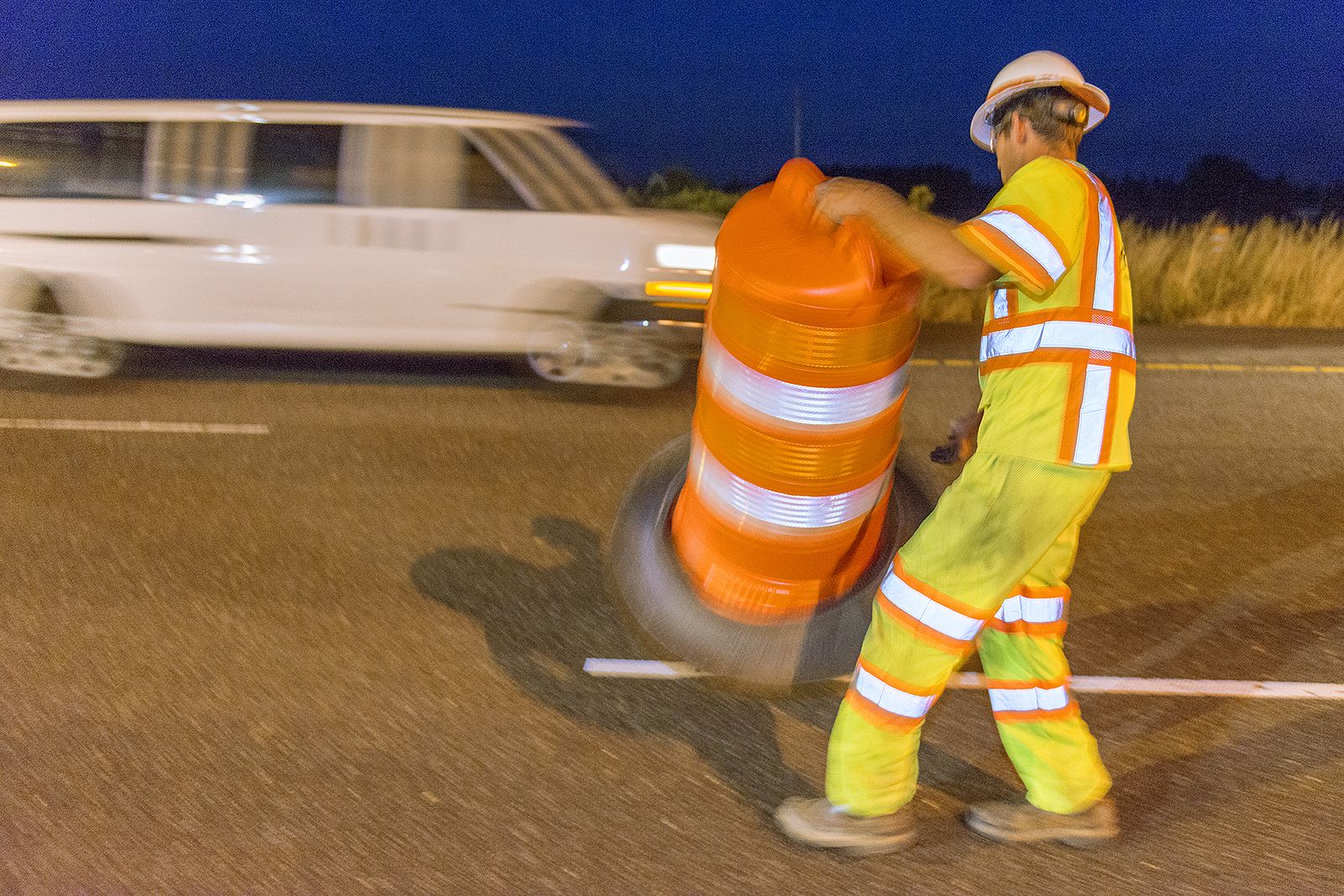 Highway worker placing work-zone barrels beside live traffic