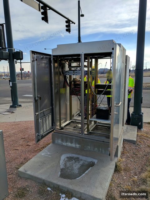 Open stainless steel roadside cabinet with equipment rack beside signal poles